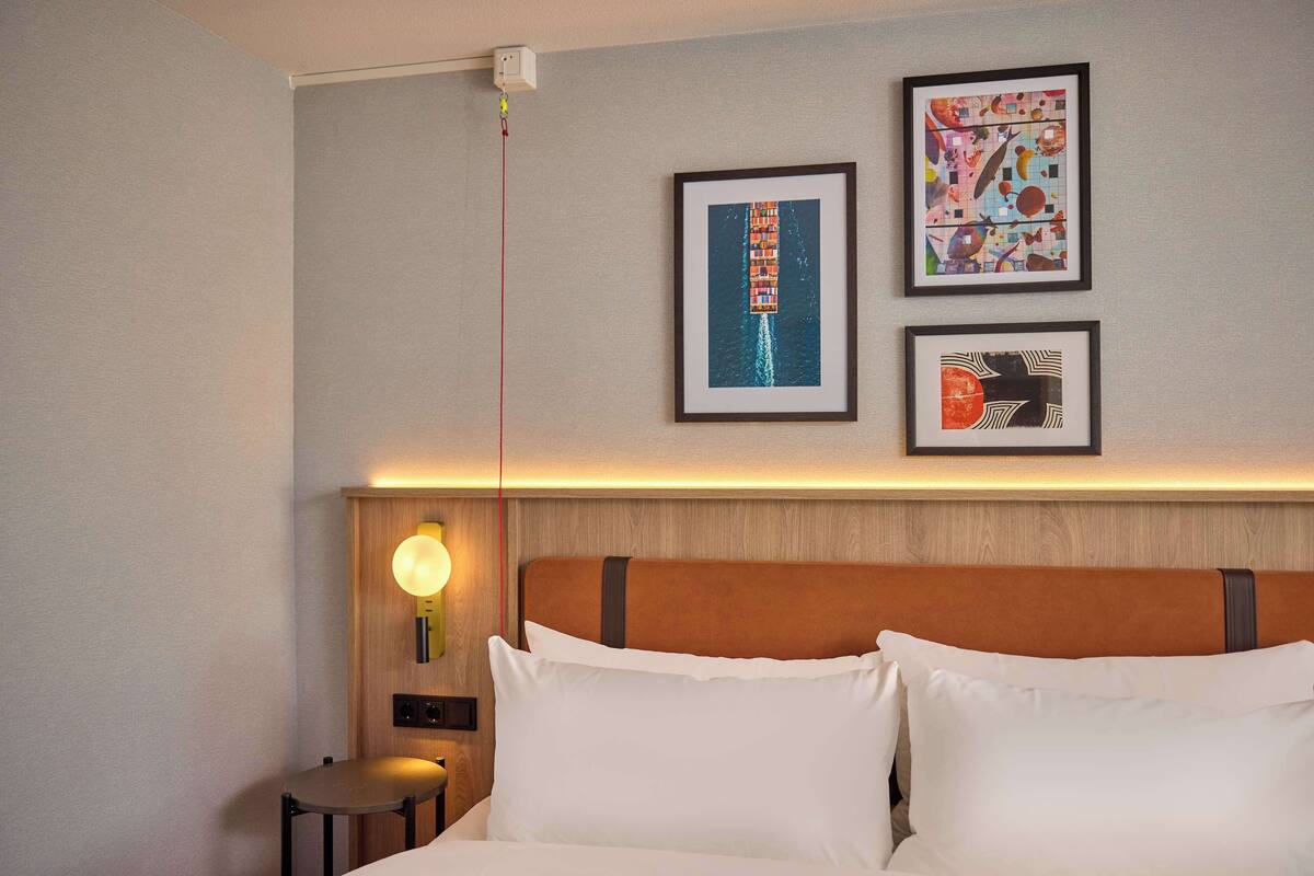 A hotel room with a bed, a nightstand, and wall-mounted artwork.