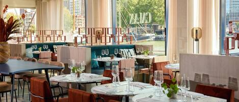 Un restaurante moderno con mesas redondas, asientos cómodos y amplios ventanales con vistas a la ciudad.