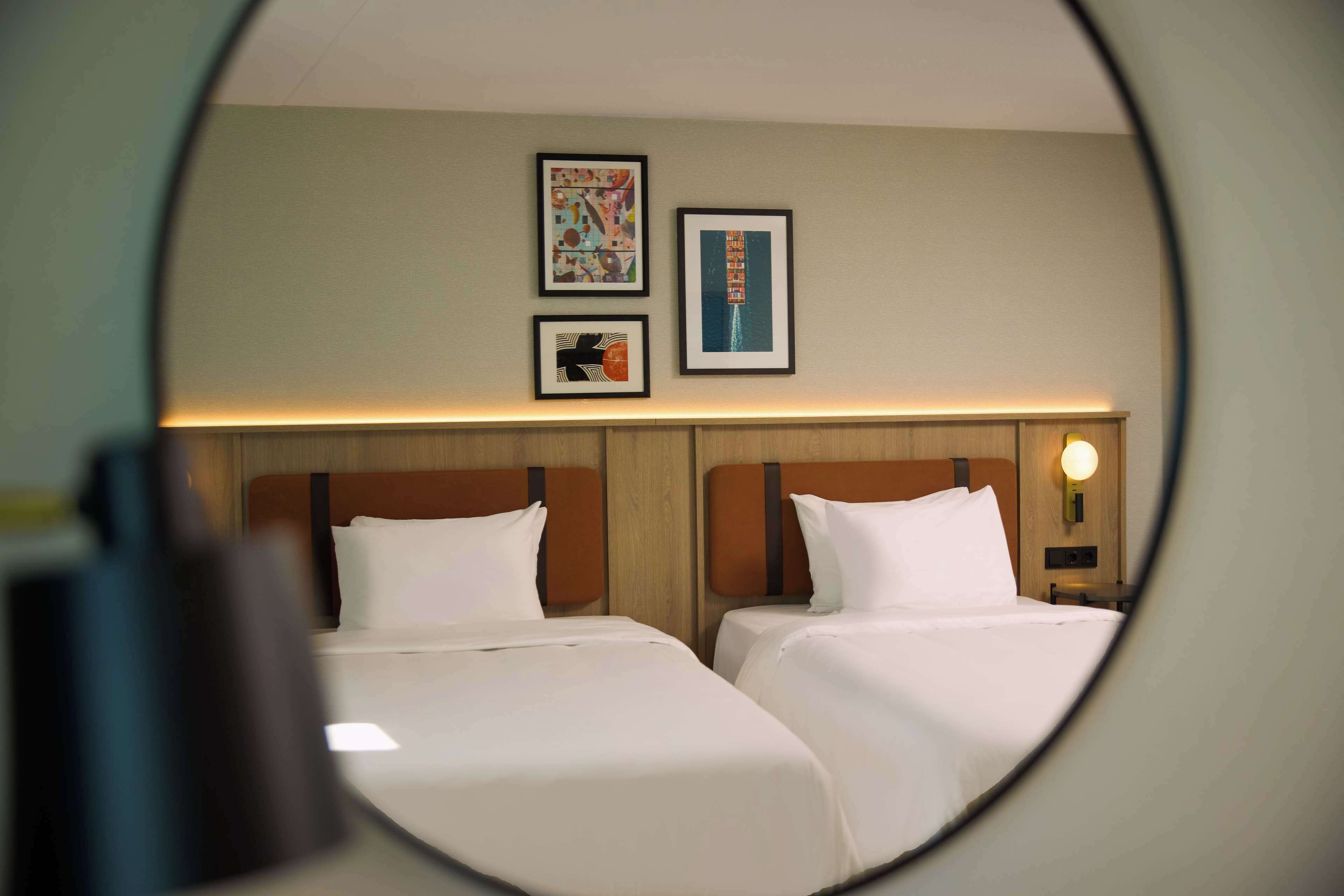 Una habitación de hotel con dos camas, un cabecero de madera y tres cuadros en la pared.
