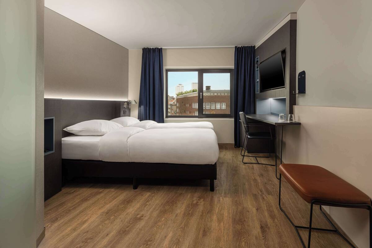 A hotel room with a bed, a desk, a bench, and a TV.