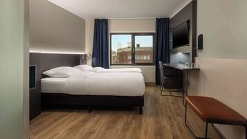 A hotel room with a bed, a desk, a bench, and a TV.