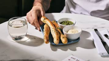 Une table avec une assiette de gressins, un verre d’eau et deux petits bols de condiments.