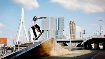 Iemand voert een skatetruc uit op een helling, met een stadsgezicht op de achtergrond.