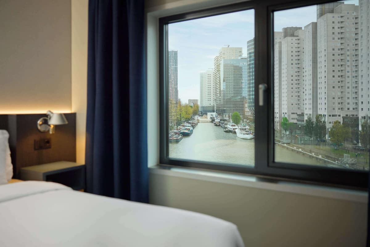 A hotel room with a large window overlooking a river and high-rise buildings.