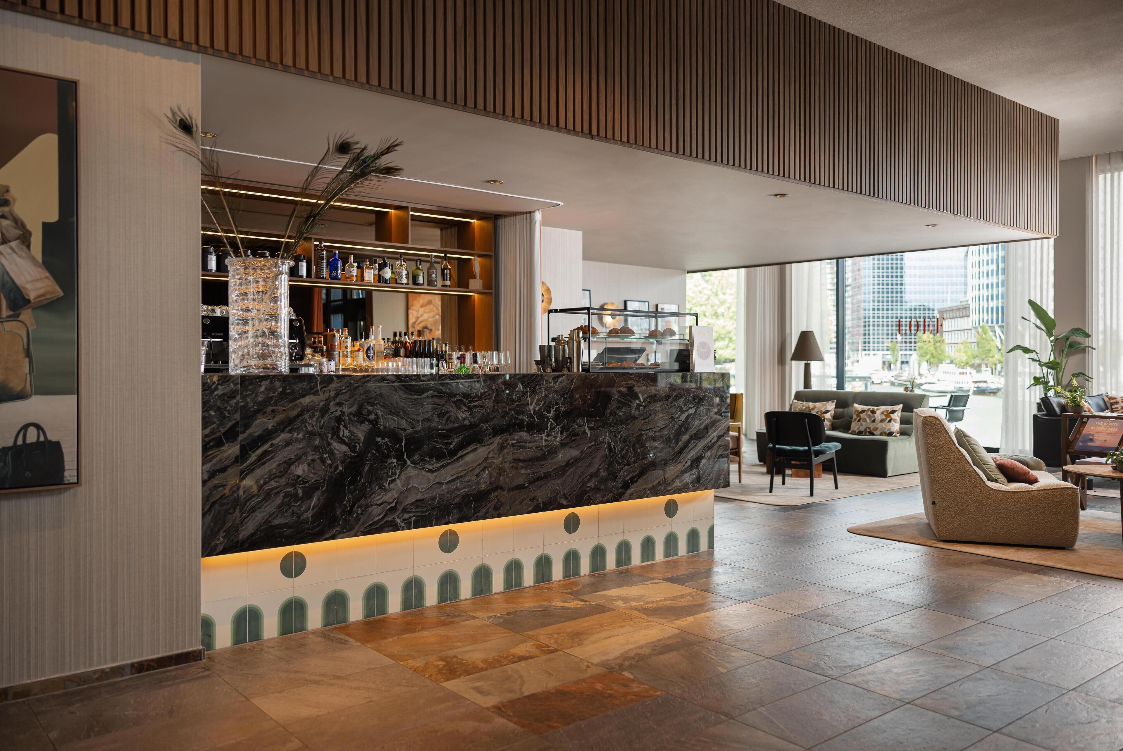 A modern hotel lobby with a marble reception desk, a bar area, and a seating area with a view of the city.