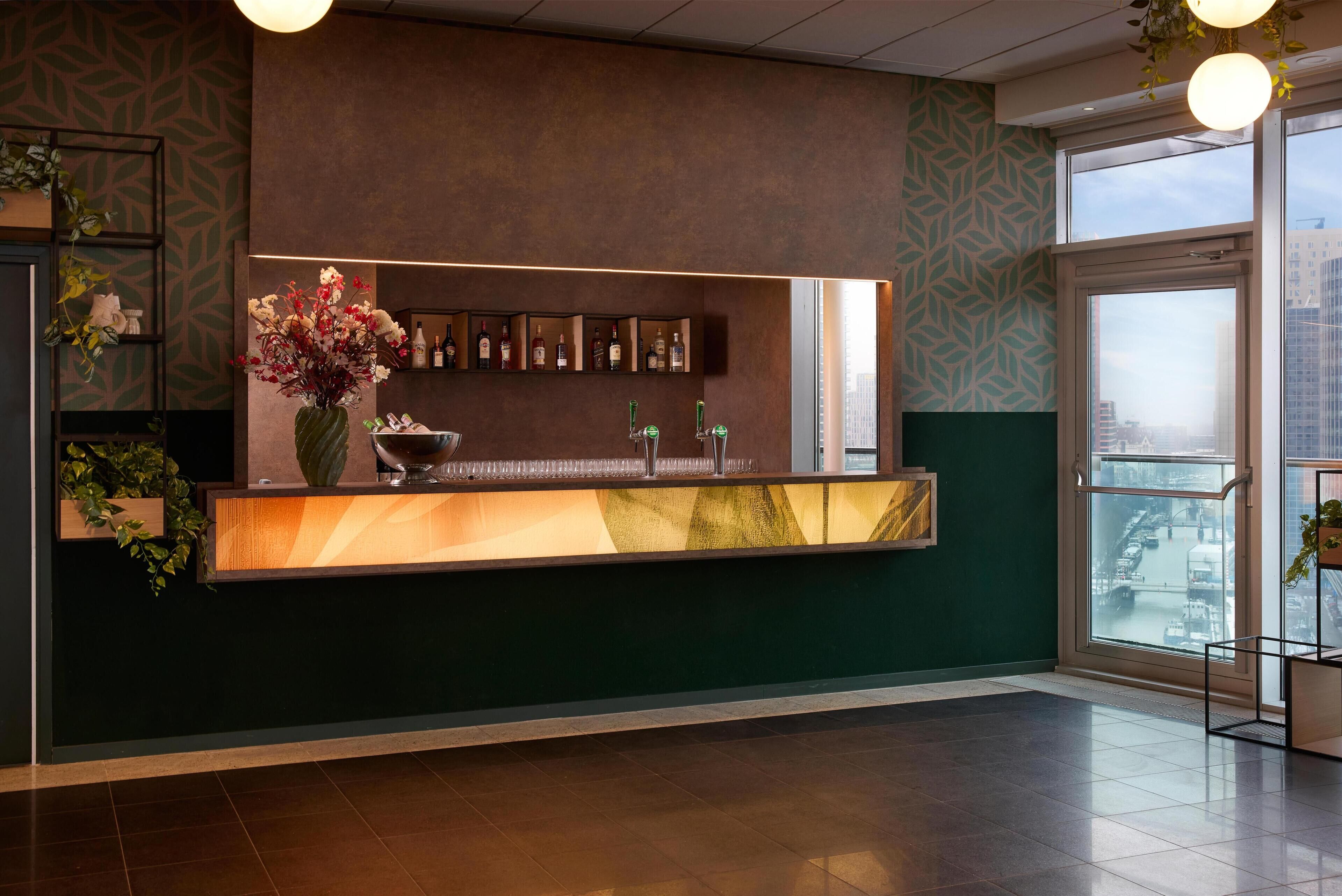 A reception area with a green and brown color scheme, a large vase of flowers, a bar counter with multiple taps, and a view of the city through large windows.
