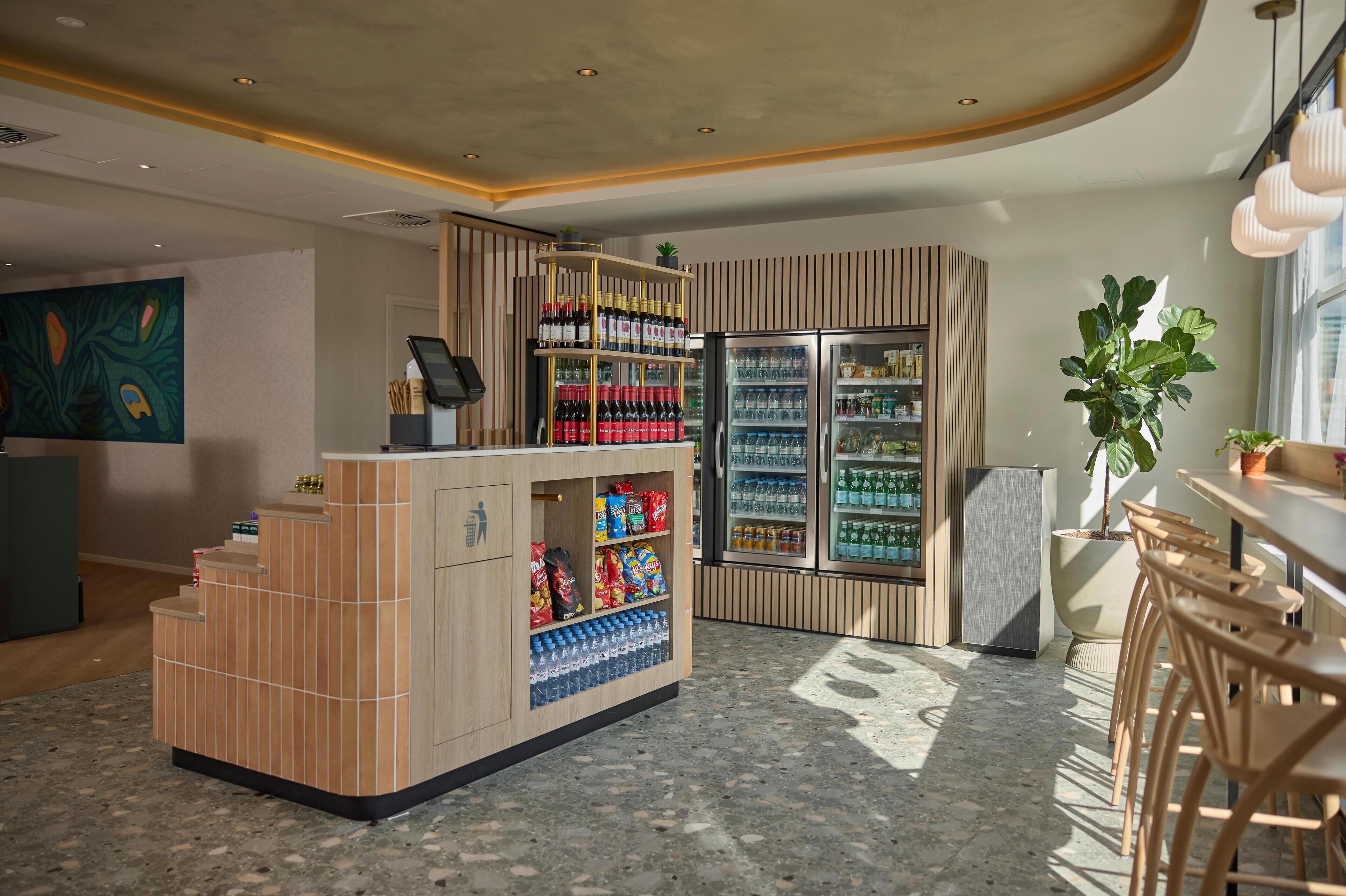 Een moderne bar met een houten toonbank, planken vol snacks en drankjes, en een koelkast.