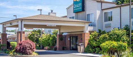 A Quality Inn & Suites with a covered entrance, brick exterior, and landscaped garden area.