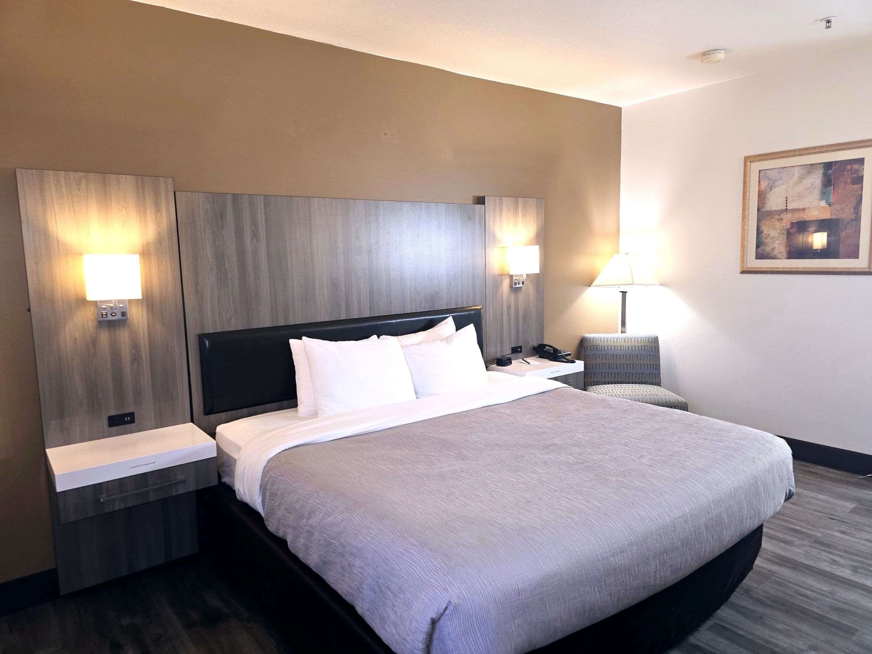A hotel room with a large bed, two bedside tables, a chair, and a painting on the wall.