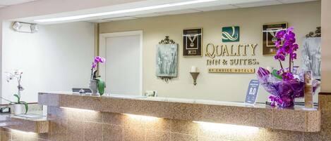 A hotel reception desk with a sign reading "QUALITY INN & SUITES BY CHOICE HOTELS".