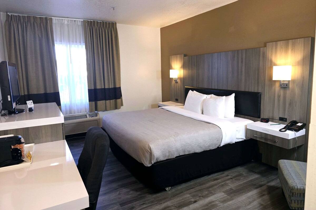 A hotel room with a large bed, bedside tables, a desk with a computer, and a chair.