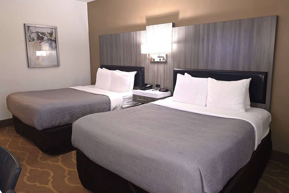 A hotel room with two beds, a bedside table with a lamp, a phone, and a painting on the wall.