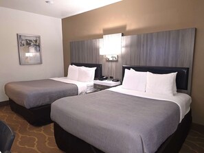 A hotel room with two beds, a bedside table with a lamp, a phone, and a painting on the wall.