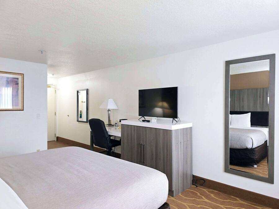 Quarto de hotel com uma cama, uma escrivaninha com televisão, uma cadeira e um espelho.
