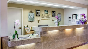 A hotel reception area with a reception desk, framed awards, and a sign indicating the hotel name and services. - Quality Inn & Suites Longview Kelso (Longview)