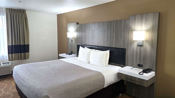 A hotel room with a large bed, two bedside tables, a headboard, and two wall-mounted lamps. - Quality Inn & Suites Longview Kelso (Longview)