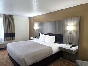 Una habitación de hotel con una cama grande, dos mesitas de noche, un cabecero y dos lámparas de pared.