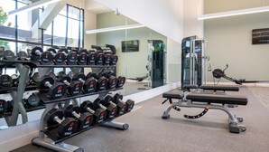 A gym with weightlifting equipment, a bench, and a mirror reflecting the interior. - The Domain Hotel (Sunnyvale)