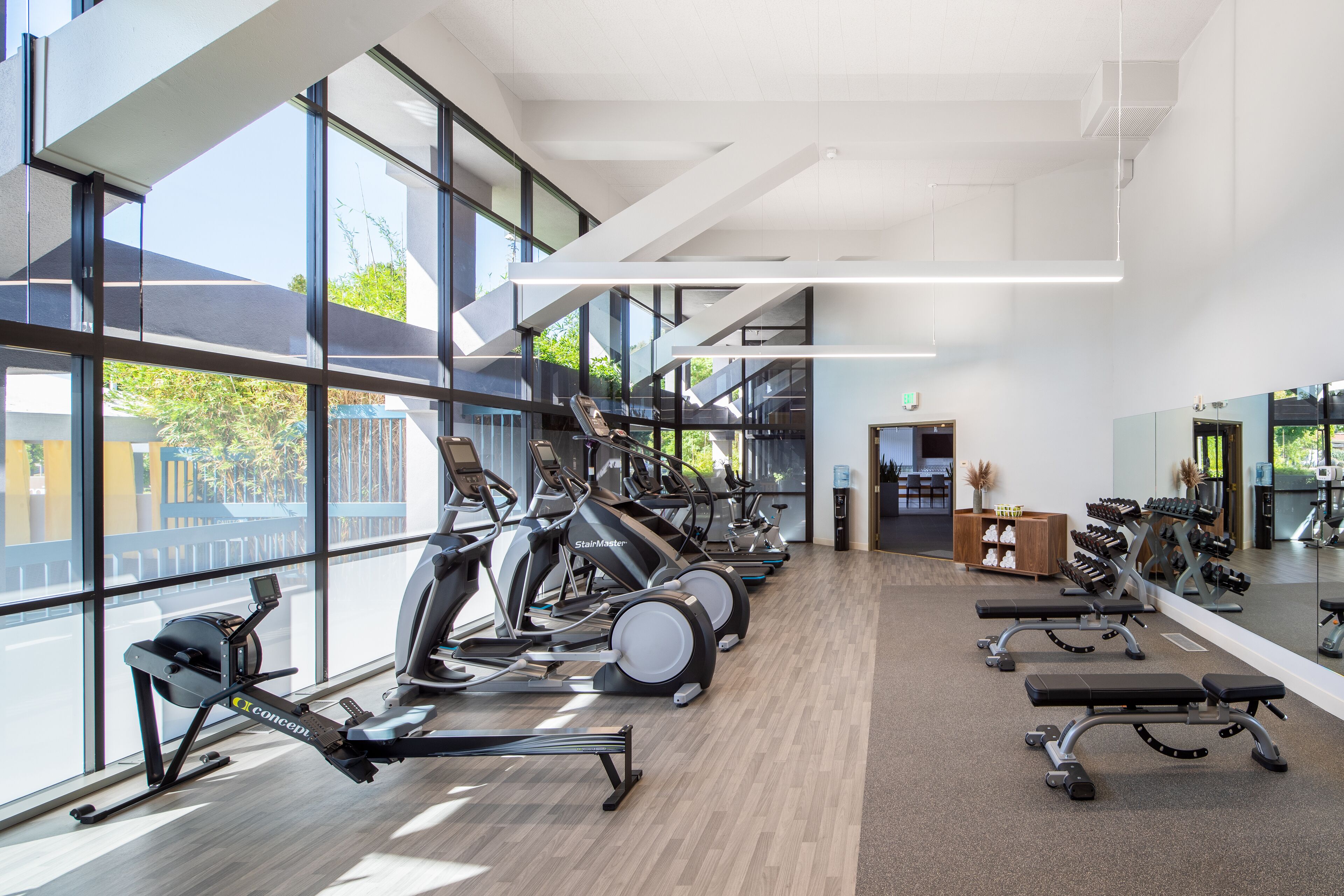 Une salle de sport moderne équipée de machines de cardio, de bancs de musculation et d’un grand miroir.
