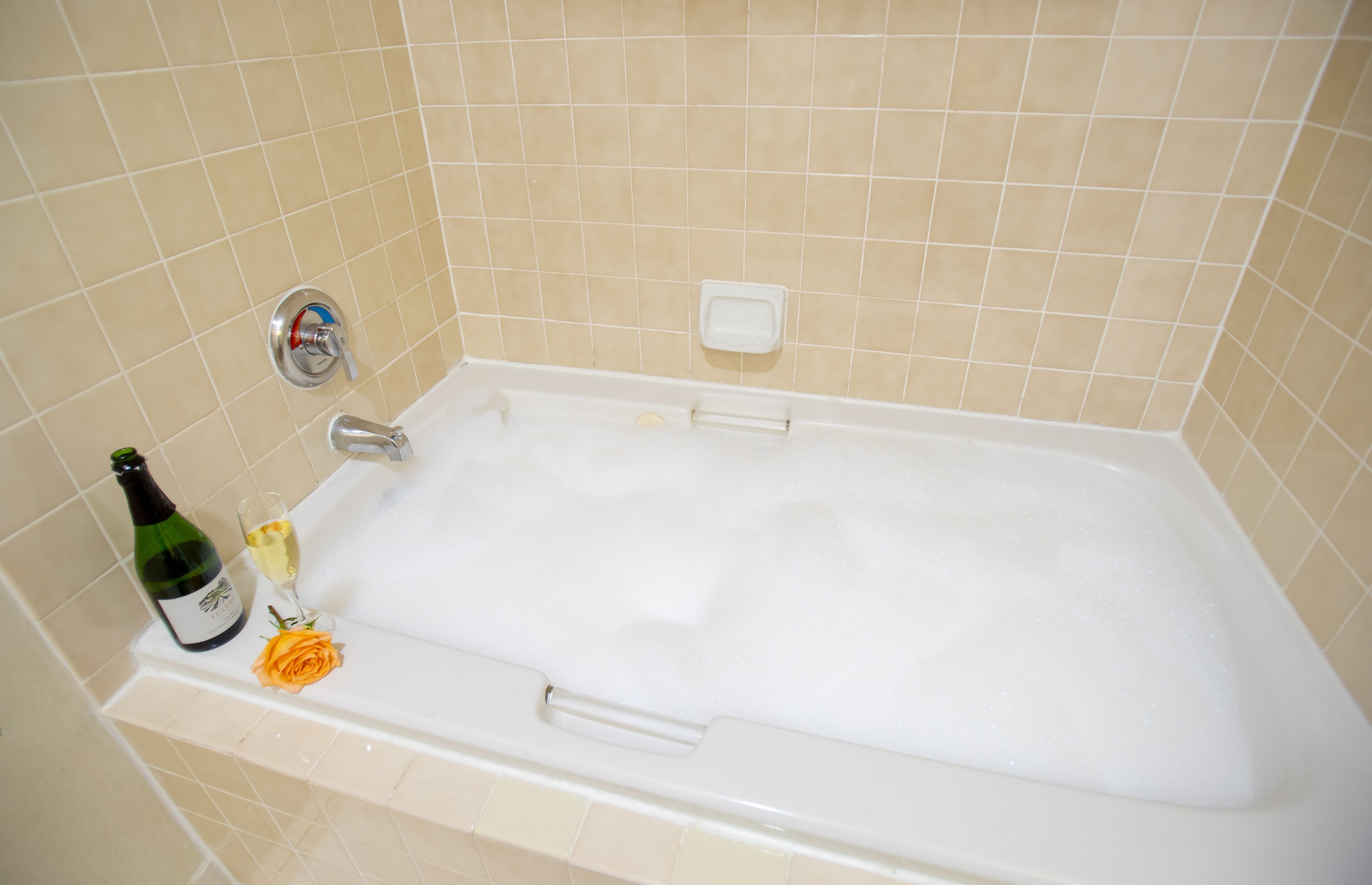 A bathtub with a bottle of champagne and a rose.