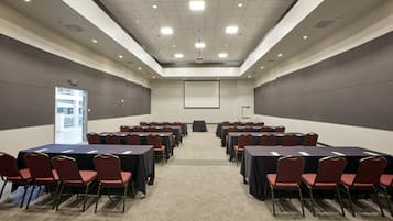 A conference room with a large screen, multiple tables, and red chairs.