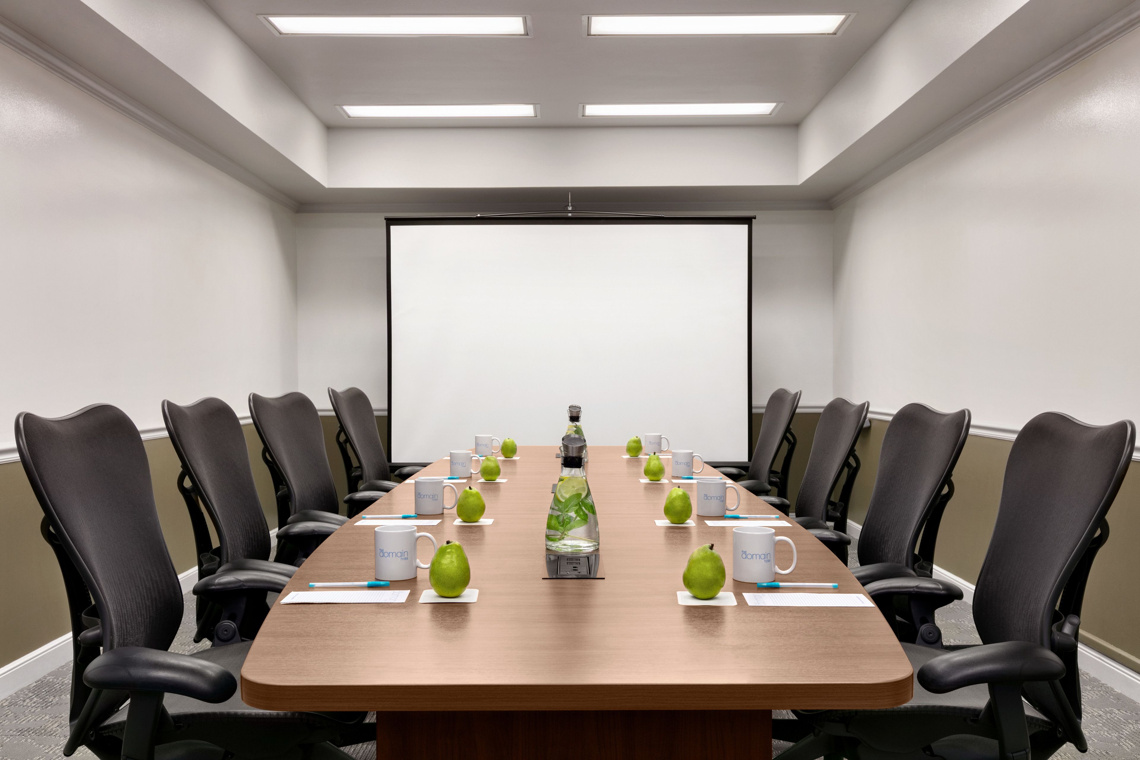 A conference room with a long table, black chairs, and a projector screen.