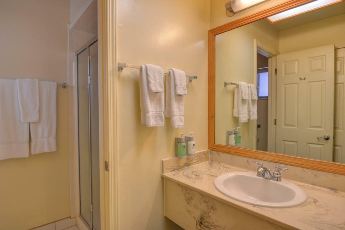 Un baño con lavamanos, espejo y toallas en un perchero.
