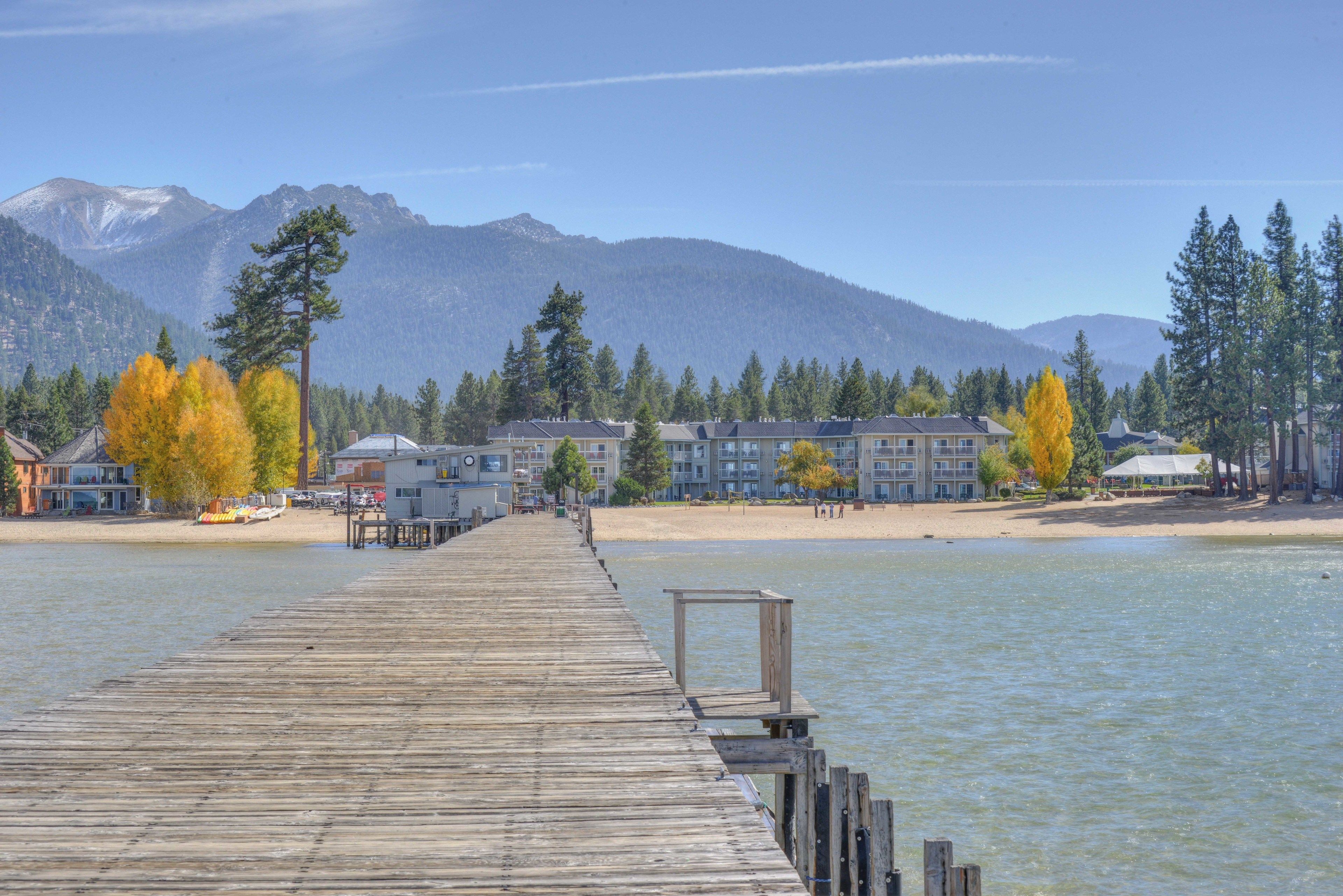 A wooden pier extending into calm water with a backdrop of mountains and autumn-colored trees.