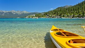 Un lac aux eaux claires, avec un canoë jaune et une pagaie au premier plan, le tout entouré de montagnes et d’arbres.