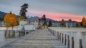 Une jetée en bois menant à un bâtiment d’où l’on peut admirer des montagnes et un coucher de soleil.