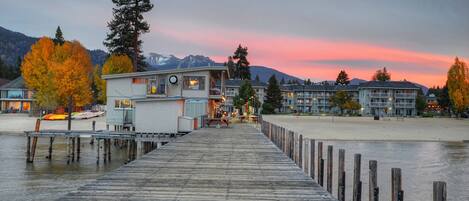 A wooden pier leading to a building with a view of mountains and a sunset.