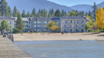 A waterfront hotel with multiple balconies, a sandy beach, and a backdrop of mountains.