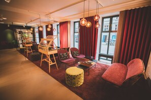 A modern interior with a wooden easel, red velvet curtains, and a view of the street outside. - Andersen Boutique Hotel (Copenhagen)