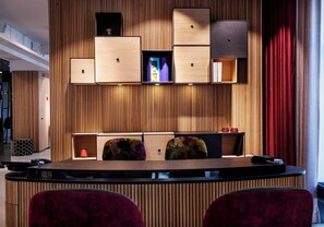 A reception desk with a wooden panel backdrop, two plush armchairs, and a red curtain to the right. - Andersen Boutique Hotel (Copenhagen)