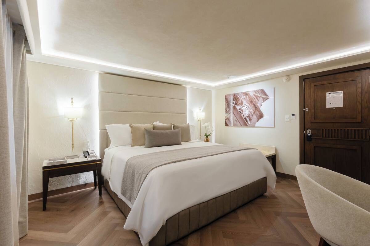 Une chambre d’hôtel avec un grand lit, des tables de chevet, une chaise et une porte.