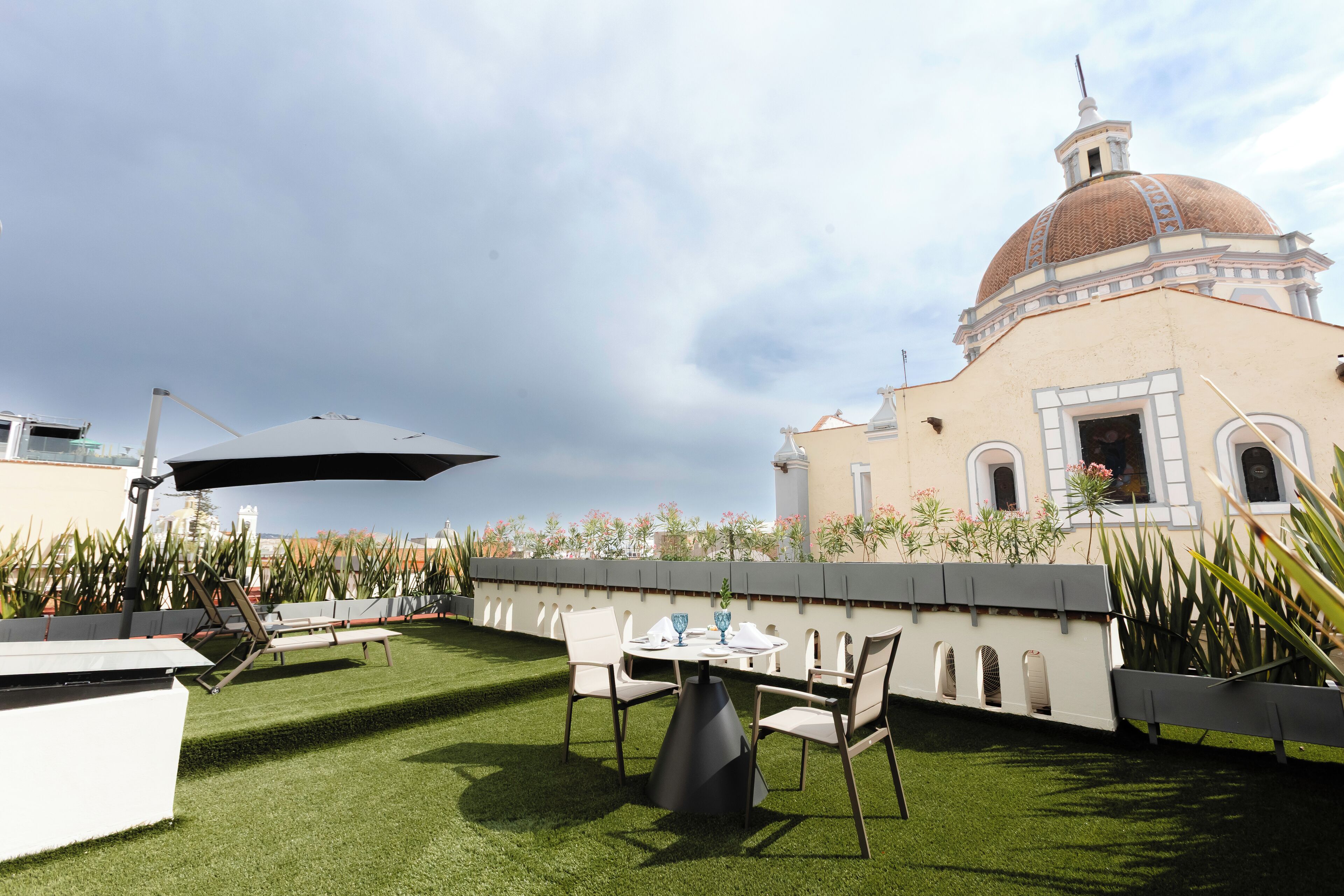 Un patio al aire libre con una mesa, sillas, un paraguas grande y un edificio con cúpula al fondo.