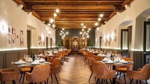 A long dining hall with wooden beams and pendant lighting, tables set with white tablecloths and orange chairs. - Quinta Real Puebla (Puebla)