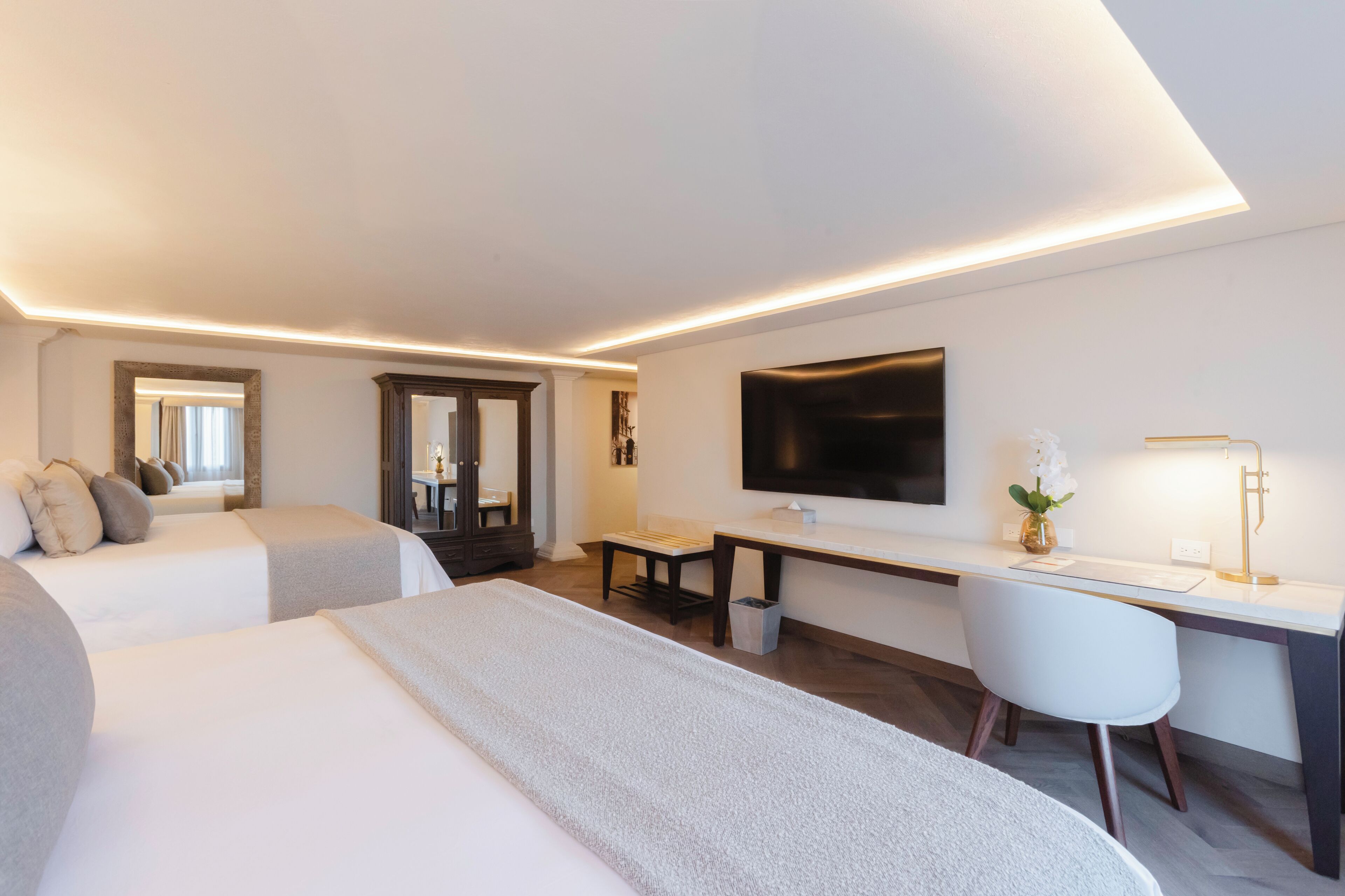 Habitación de hotel con dos camas, un escritorio, una silla, un televisor y una mesita de noche con lámpara.