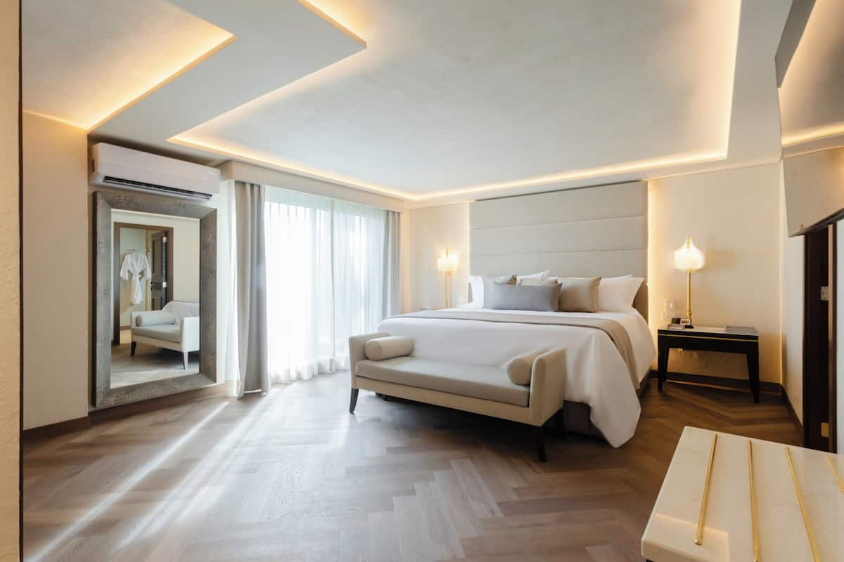 Une chambre d’hôtel moderne, dotée d’un grand lit, de tables de chevet, d’un miroir et offrant une vue sur l’extérieur.