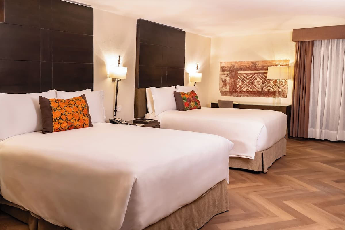 Une chambre d’hôtel avec deux lits, chacun agrémenté de draps blancs et d’oreillers décoratifs. On y trouve des lampes fixées au mur et un élément décoratif mural.