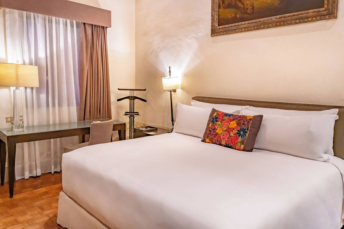 Une chambre d’hôtel avec un lit, un bureau, une chaise, une lampe et un tableau au mur.
