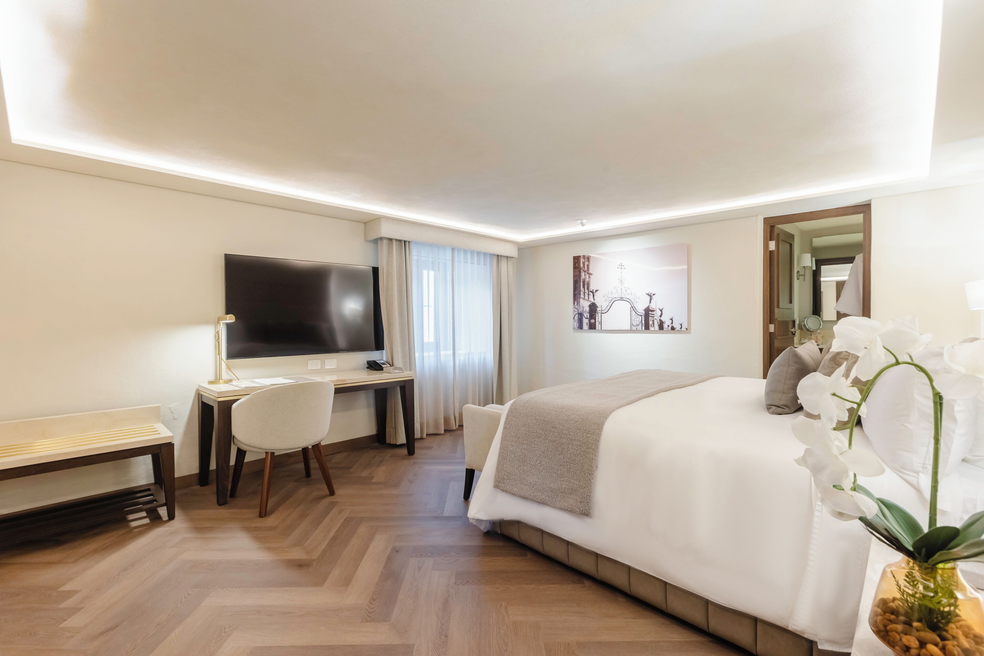 Une chambre d’hôtel équipée d’un lit, d’un bureau, d’une chaise, d’une télévision et d’une grande fenêtre avec des rideaux.