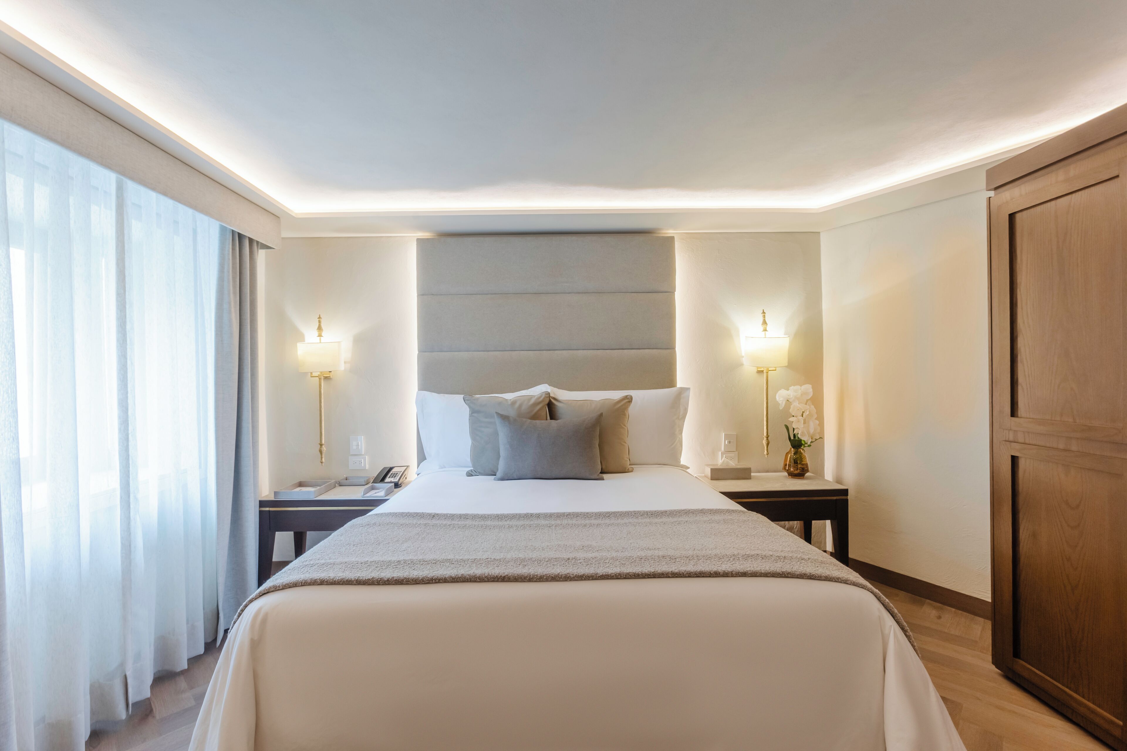 A hotel room with a large bed, two bedside tables, a nightstand, a lamp, and a vase with flowers.