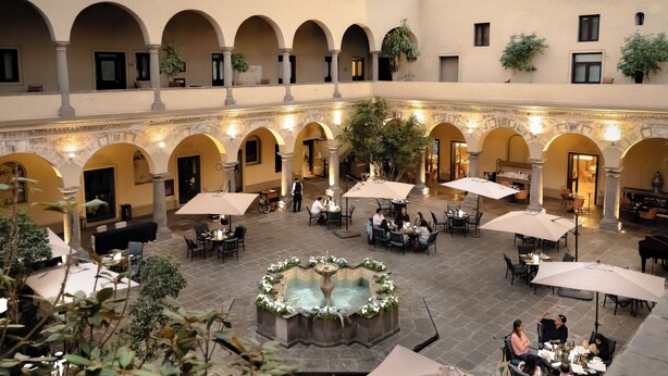 An indoor courtyard with multiple dining areas, a central fountain, and arches. - Quinta Real Puebla (Puebla)