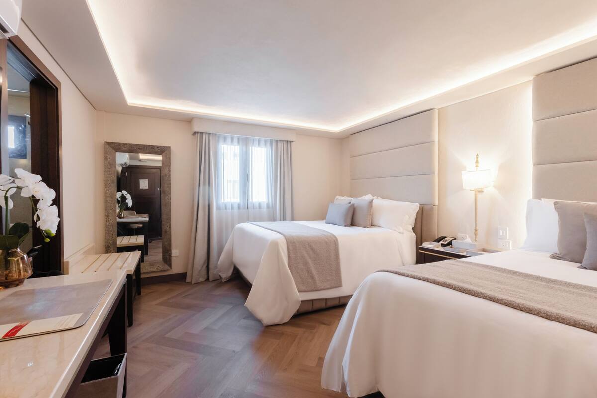 Une chambre d’hôtel avec deux lits, un bureau, un miroir et une lampe.