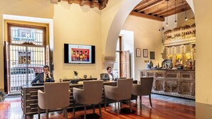 A hotel lobby with a wooden reception desk, a television mounted on the wall, and a bar area with ornate decorations. - Quinta Real Puebla (Puebla)