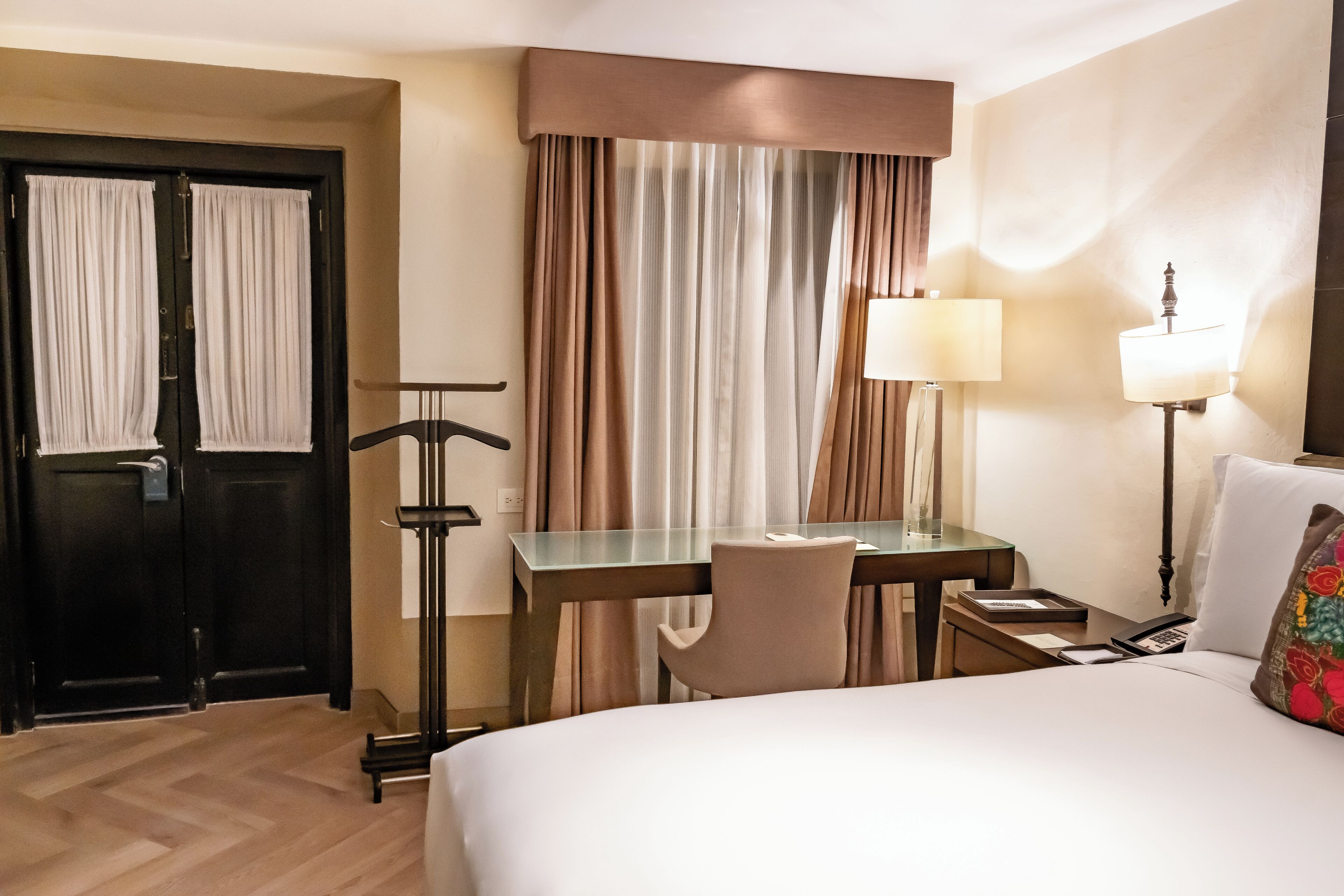 Una habitación de hotel con cama, escritorio, silla, lámpara y armario.
