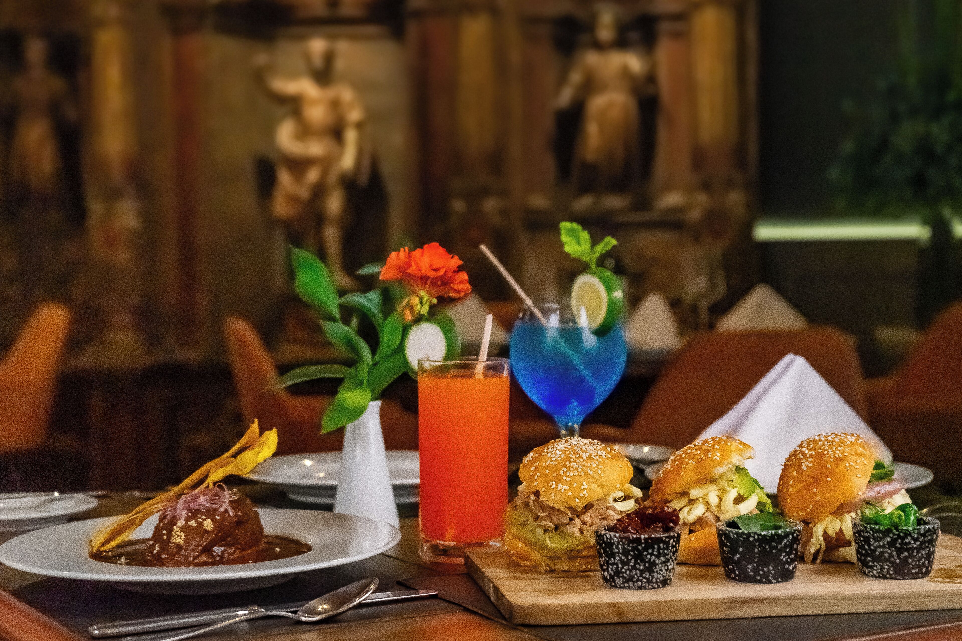 A dining table with a dessert, two burgers, a cocktail, and small cups of sauce.