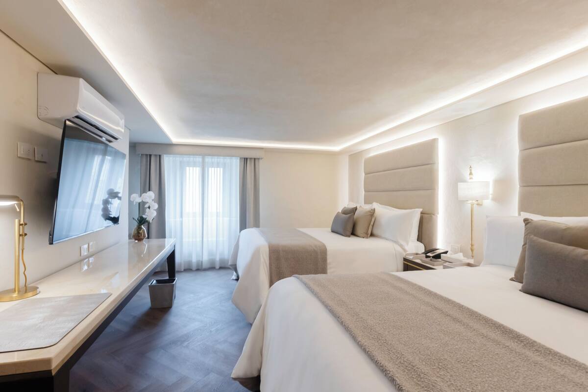 Une chambre d’hôtel avec deux lits, un bureau, une télévision et une table de chevet avec une lampe.