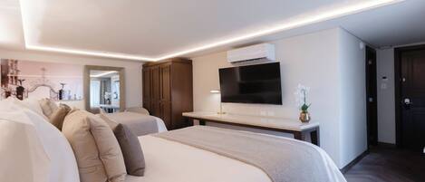 A modern hotel room with two beds, a flat-screen TV, an air conditioning unit, and a small table with a vase.
